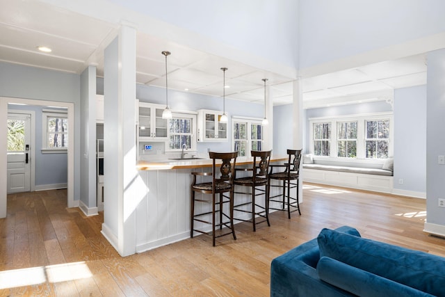 kitchen with a breakfast bar, a sink, glass insert cabinets, light wood-style floors, and white cabinetry