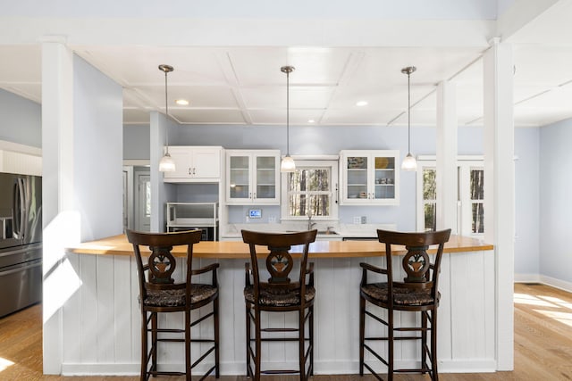 kitchen with wood finished floors, stainless steel fridge with ice dispenser, glass insert cabinets, white cabinetry, and butcher block counters