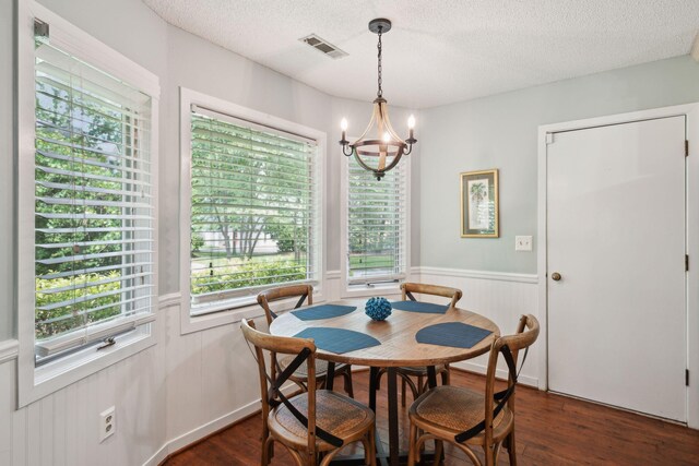 dining room with dark wood-type flooring, a chandelier, a textured ceiling, and wainscoting