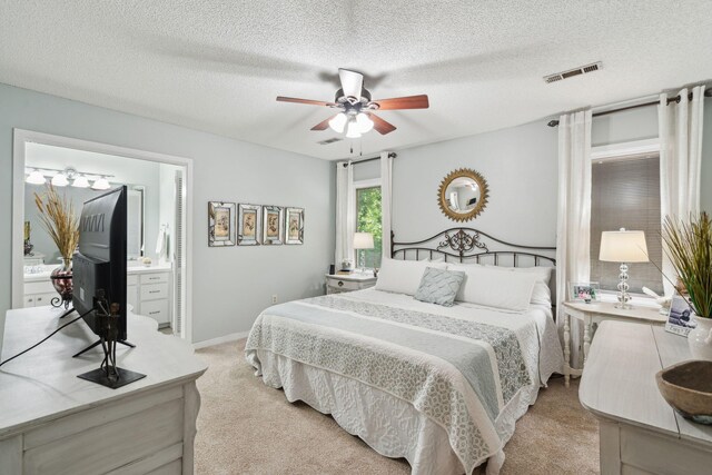 bedroom with light colored carpet, a textured ceiling, ceiling fan, and connected bathroom
