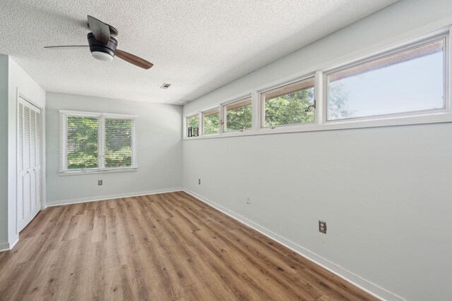 unfurnished bedroom featuring wood finished floors, a textured ceiling, baseboards, a ceiling fan, and a closet