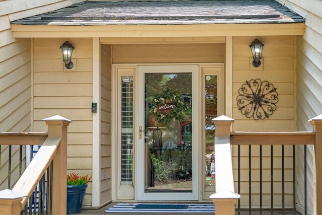 view of exterior entry featuring a shingled roof and a porch