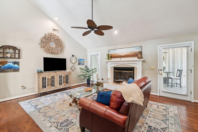 living area featuring ceiling fan, a fireplace, wood finished floors, baseboards, and high vaulted ceiling