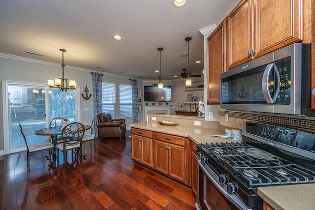 kitchen featuring appliances with stainless steel finishes, dark hardwood / wood-style flooring, ornamental molding, ceiling fan with notable chandelier, and hanging light fixtures