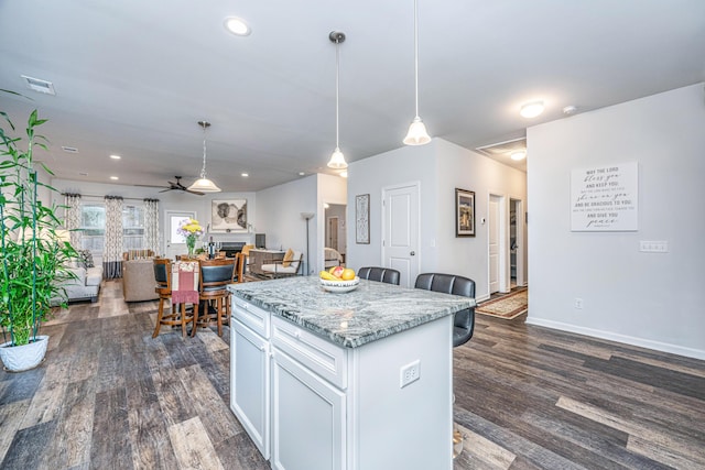 kitchen featuring light stone counters, ceiling fan, pendant lighting, white cabinets, and a kitchen island