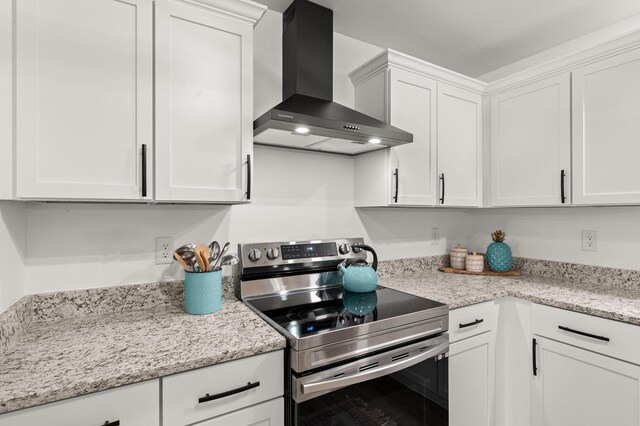 kitchen with electric stove, wall chimney range hood, white cabinetry, and light stone counters