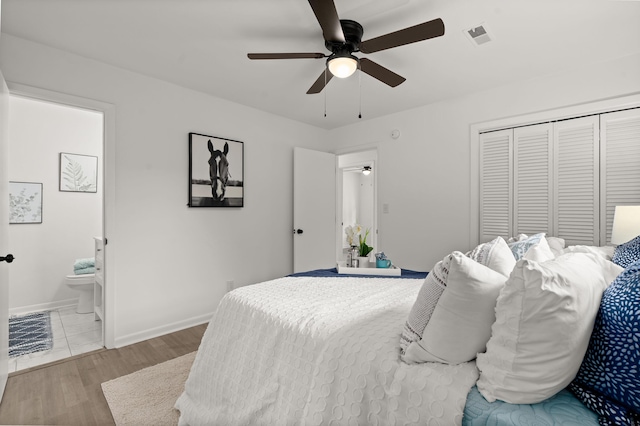 bedroom featuring baseboards, wood finished floors, a closet, ensuite bathroom, and a ceiling fan