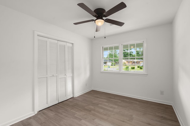 unfurnished bedroom featuring wood finished floors, a closet, baseboards, and ceiling fan