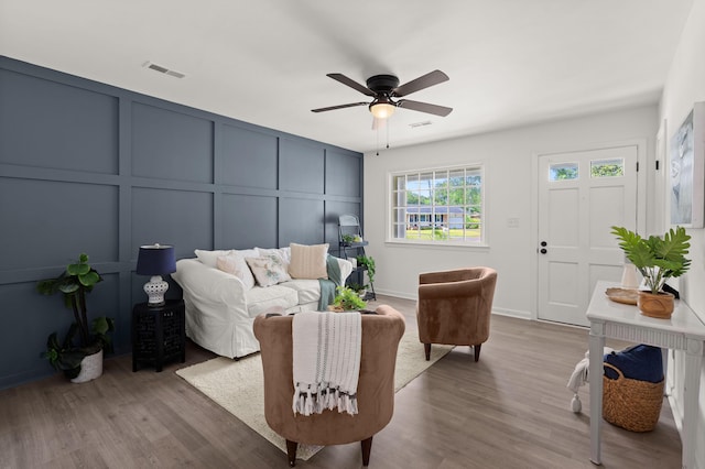 living area with a decorative wall, a ceiling fan, and wood finished floors