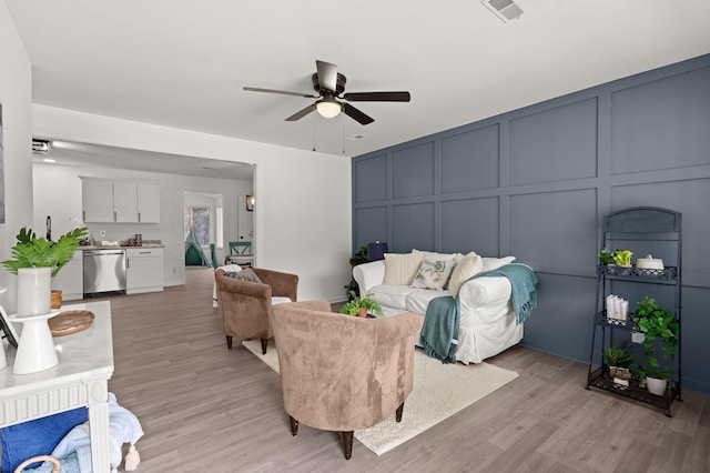 living area featuring a decorative wall, ceiling fan, and light wood-type flooring