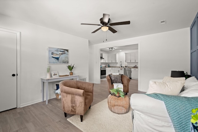 living area featuring light wood-type flooring, ceiling fan, and baseboards