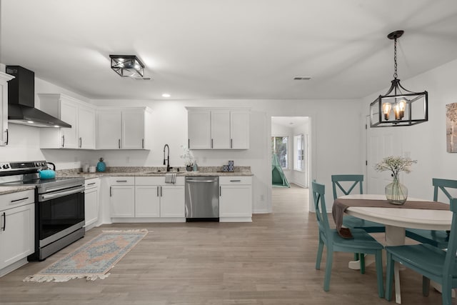 kitchen featuring stainless steel appliances, wall chimney exhaust hood, a chandelier, a sink, and white cabinets