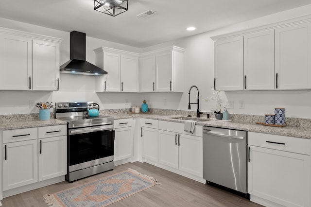kitchen featuring stainless steel appliances, wall chimney exhaust hood, a sink, white cabinets, and light wood finished floors