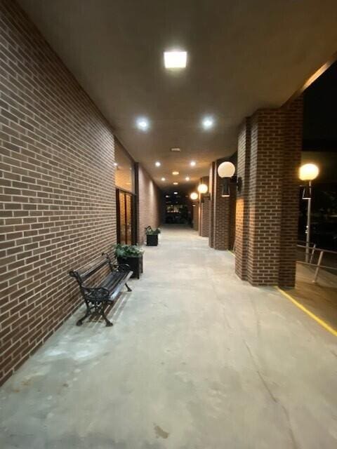 hallway featuring brick wall, concrete flooring, and recessed lighting