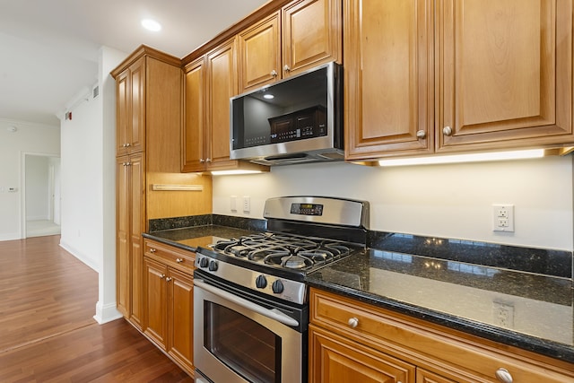 kitchen featuring dark stone countertops, stainless steel appliances, brown cabinets, and dark wood-style floors