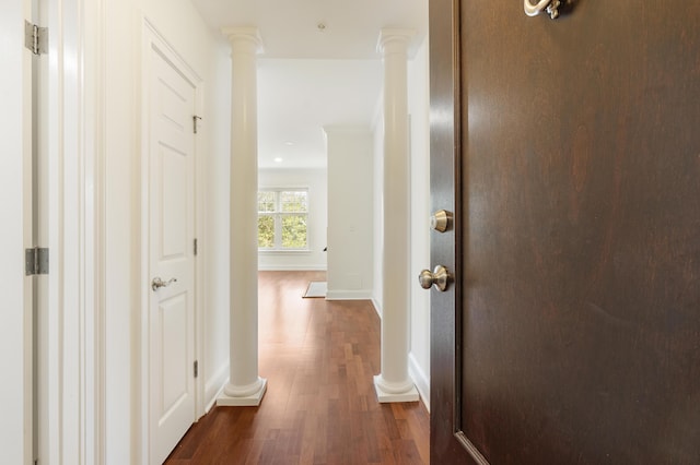 hall featuring dark wood-style floors, baseboards, and ornate columns