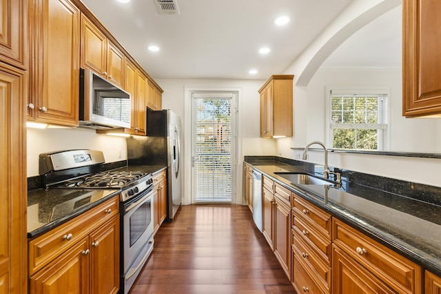 kitchen with visible vents, a sink, dark stone counters, stainless steel appliances, and dark wood-style flooring