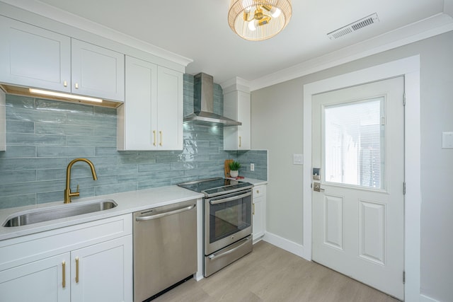 kitchen with sink, wall chimney range hood, light hardwood / wood-style flooring, white cabinets, and appliances with stainless steel finishes