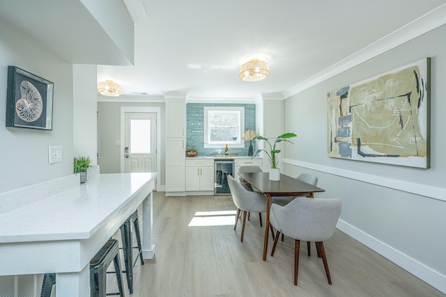 dining space with light wood-type flooring, crown molding, and beverage cooler