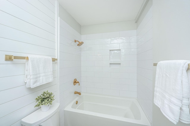 bathroom featuring tiled shower / bath combo, wood walls, and toilet