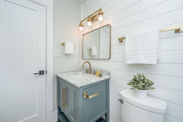 bathroom with vanity, toilet, and wooden walls