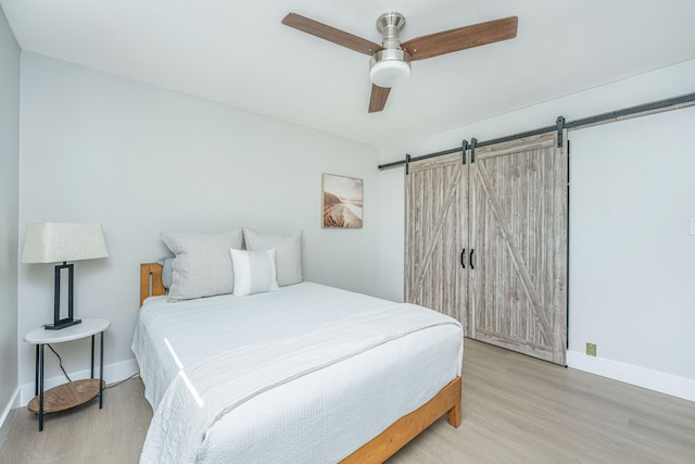 bedroom with hardwood / wood-style floors, ceiling fan, and a barn door