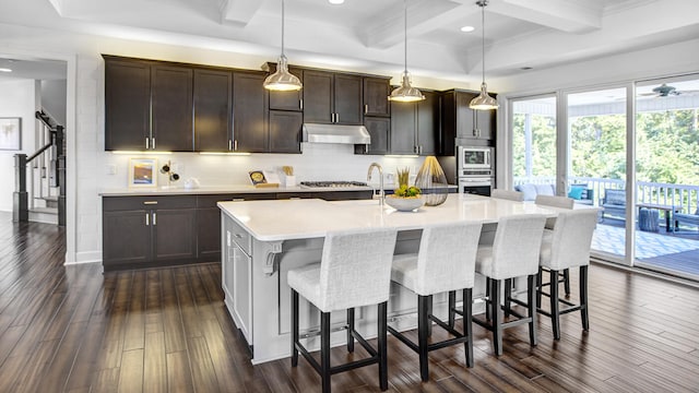 kitchen featuring a center island with sink, beam ceiling, dark hardwood / wood-style flooring, and pendant lighting