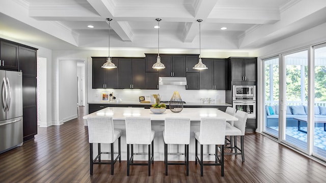 kitchen featuring an island with sink, backsplash, appliances with stainless steel finishes, and decorative light fixtures