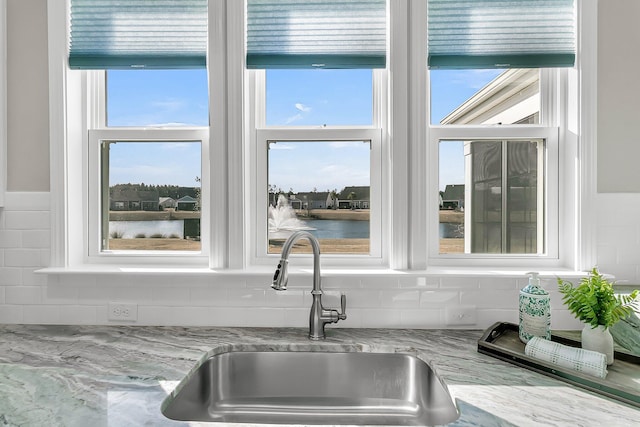 details with light stone counters, a water view, sink, and tasteful backsplash