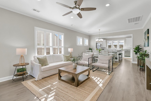 living room with ornamental molding, ceiling fan with notable chandelier, and light wood-type flooring