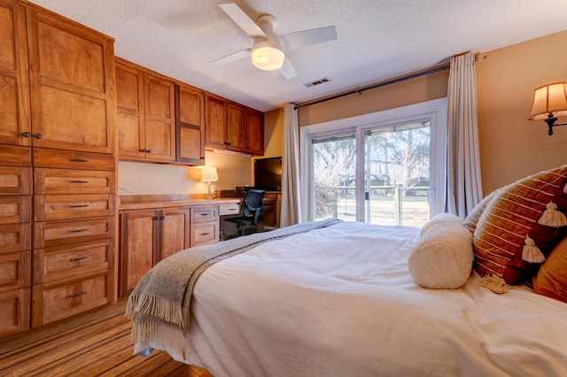 bedroom featuring visible vents, light wood-style flooring, a textured ceiling, built in desk, and access to exterior