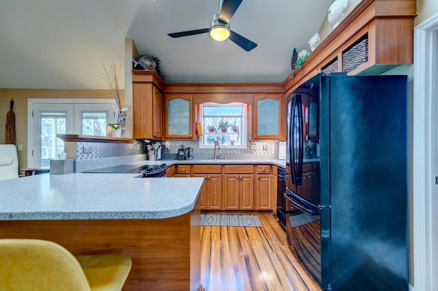 kitchen with light countertops, light wood-style flooring, a peninsula, freestanding refrigerator, and a ceiling fan