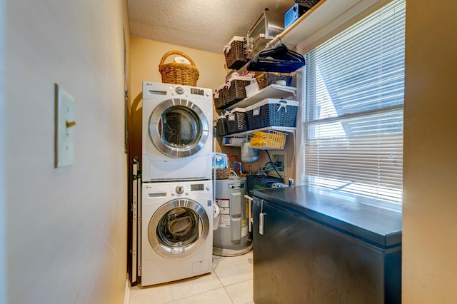 clothes washing area featuring electric water heater, stacked washer and dryer, light tile patterned floors, laundry area, and a textured ceiling