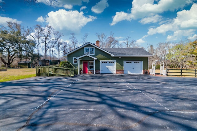 view of front facade featuring driveway, a gate, fence, a garage, and a chimney