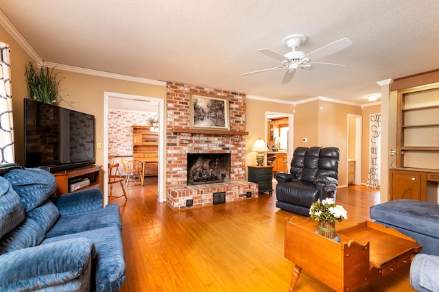 living room with ornamental molding, a textured ceiling, wood finished floors, a brick fireplace, and ceiling fan