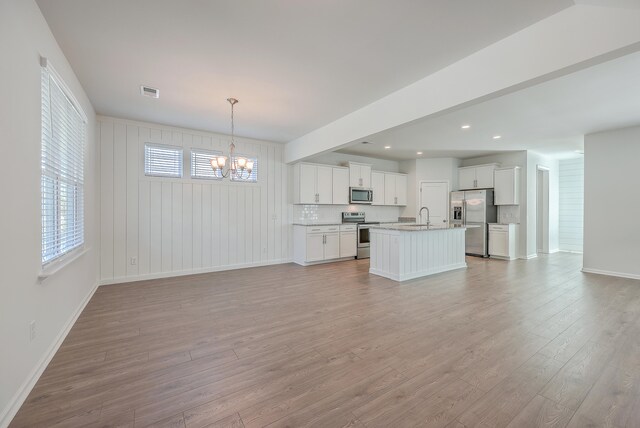 kitchen with tasteful backsplash, hanging light fixtures, a center island with sink, appliances with stainless steel finishes, and a notable chandelier