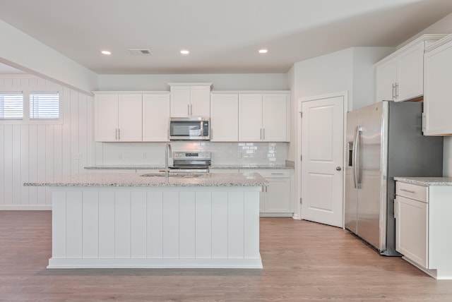 kitchen with appliances with stainless steel finishes, an island with sink, and white cabinets