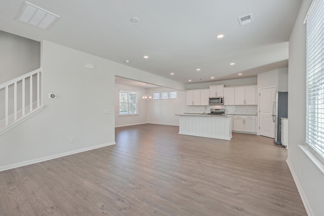 kitchen with appliances with stainless steel finishes, tasteful backsplash, white cabinets, light hardwood / wood-style floors, and a center island with sink