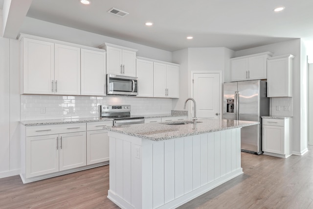 kitchen featuring sink, white cabinetry, a center island with sink, stainless steel appliances, and light stone countertops