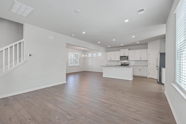 kitchen featuring backsplash, stainless steel appliances, light hardwood / wood-style floors, an island with sink, and white cabinets