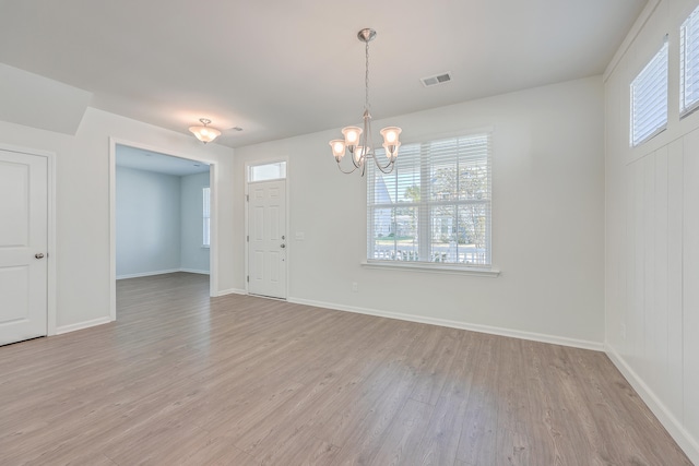 spare room with a notable chandelier and light wood-type flooring