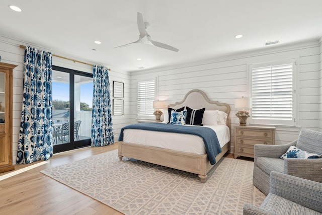 bedroom with ceiling fan, light hardwood / wood-style floors, wood walls, and access to outside