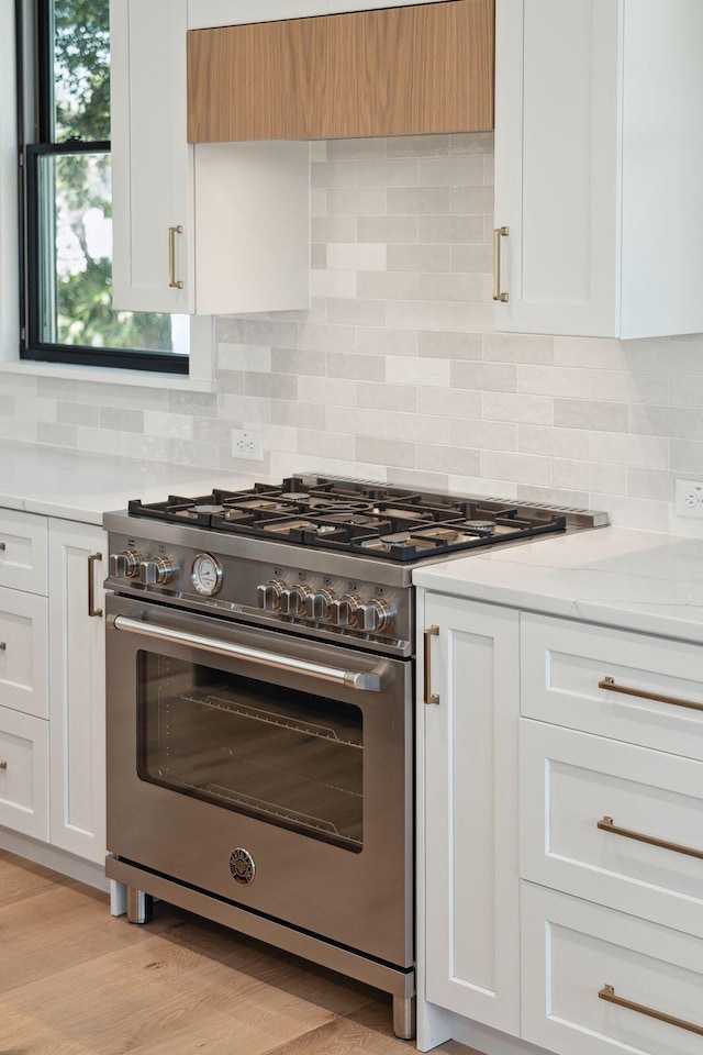 kitchen with high end stove, decorative backsplash, white cabinetry, light stone countertops, and ventilation hood