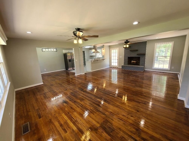 unfurnished living room featuring a brick fireplace, dark wood-type flooring, a wealth of natural light, and ceiling fan