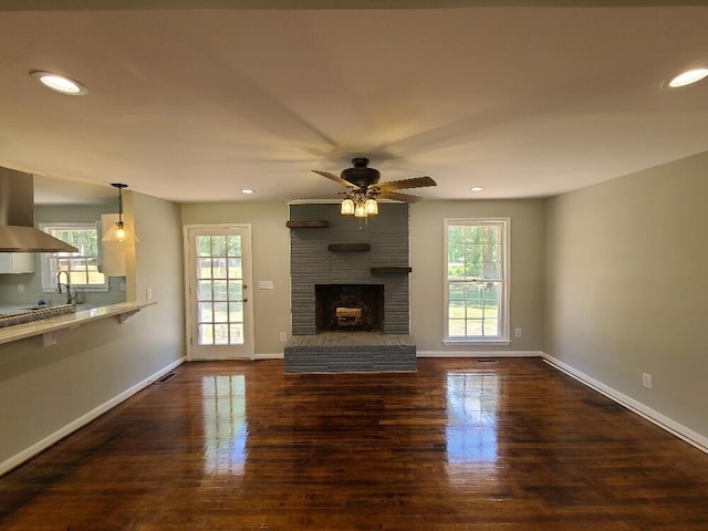 unfurnished living room featuring a healthy amount of sunlight, dark hardwood / wood-style floors, ceiling fan, and a fireplace