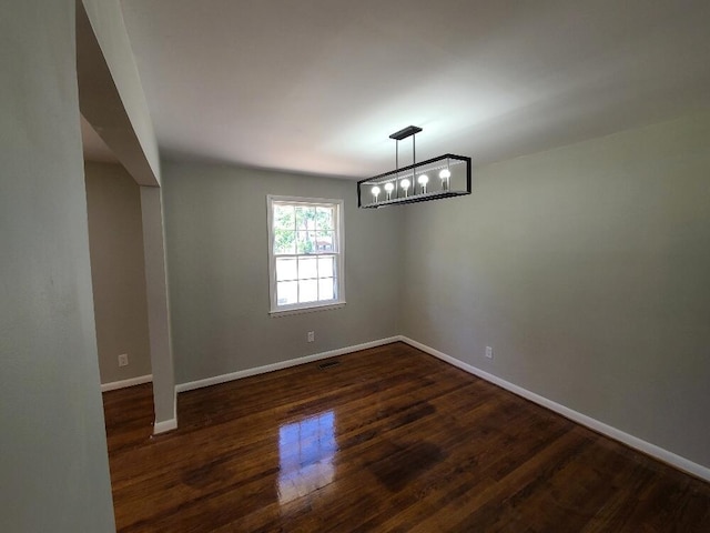 spare room featuring dark wood-type flooring and a notable chandelier