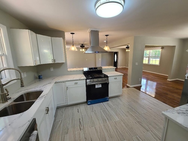 kitchen featuring pendant lighting, island range hood, white cabinetry, sink, and stainless steel gas range oven