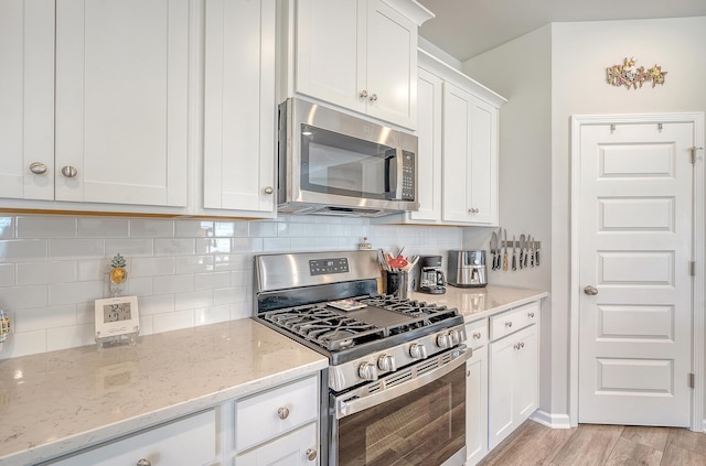 kitchen with light hardwood / wood-style flooring, backsplash, white cabinets, appliances with stainless steel finishes, and light stone counters