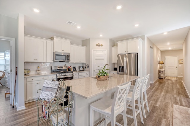 kitchen with white cabinetry, light hardwood / wood-style floors, stainless steel appliances, and a kitchen island with sink