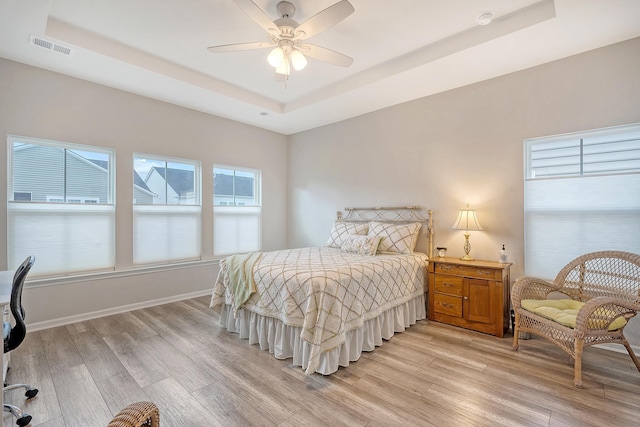 bedroom with a raised ceiling, light wood-type flooring, and ceiling fan